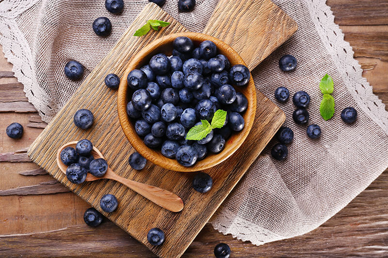 Wooden bowl of blueberries on cutting board on sacking napkin on wooden background