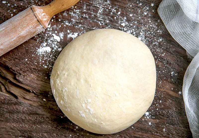 Raw dough for bread or pizza on a dark background.