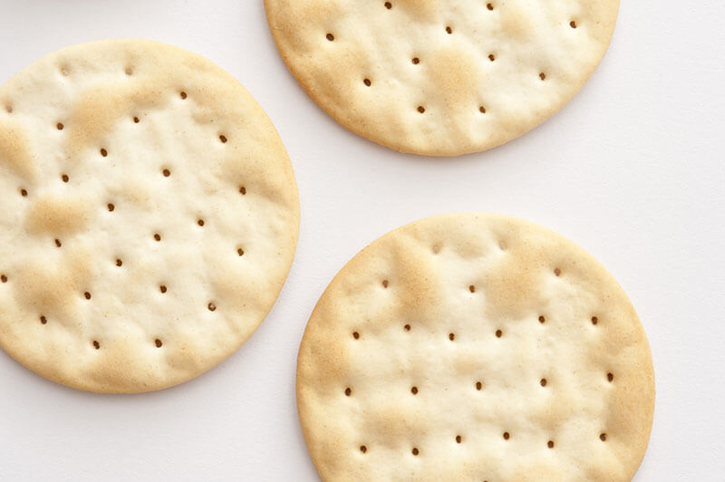 Water crackers background with an overhead view of plain crispy water biscuits made from flour and water served to accompany a cheese platter, on white