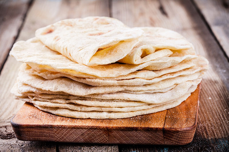 Stack of homemade wheat tortillas on wooden table