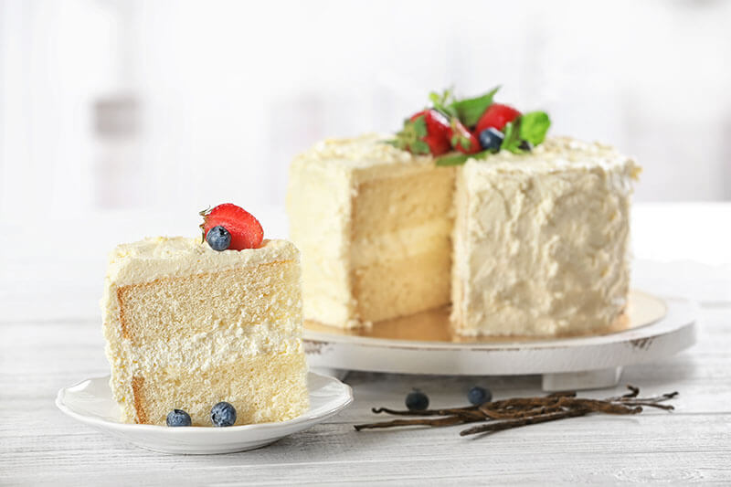 Sliced delicious vanilla cake with fresh berries on wooden table