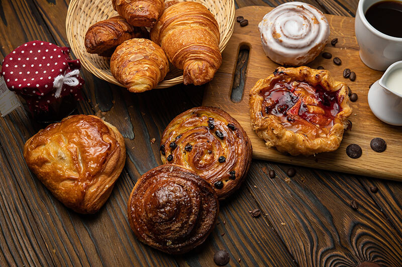 Assorted pastries, croissants, buns. On a brown wooden table.