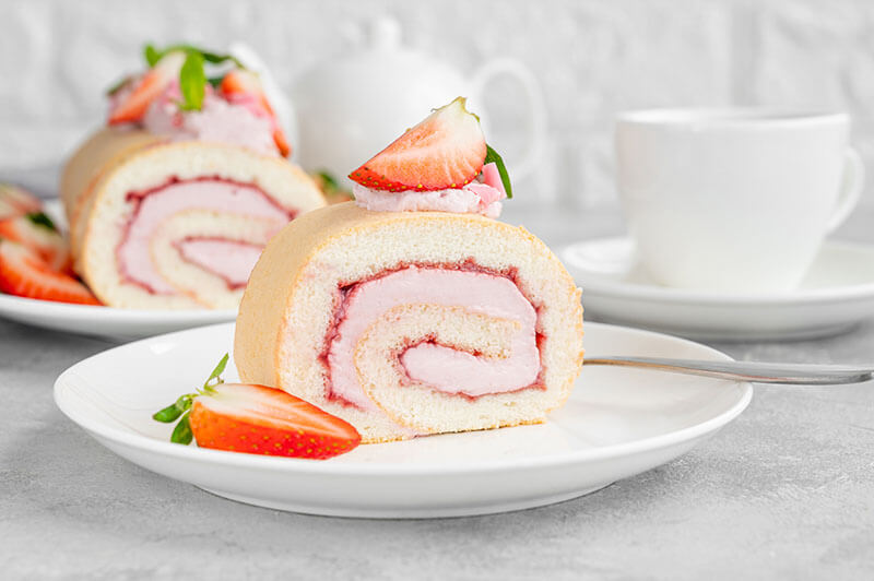 Cake roll with fresh strawberries, jam and cream cheese on a white plate on a gray background. Copy space