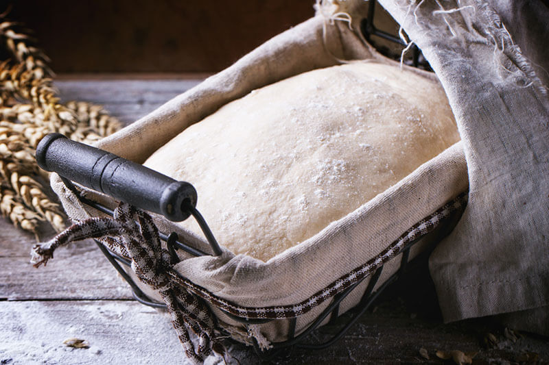 Baking bread. Dough in proofing basket on wooden table with flour and wheat ears.