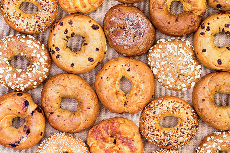 Assorted variety of different flavored freshly baked bagels in a full frame background on burlap viewed from above in an abstract pattern